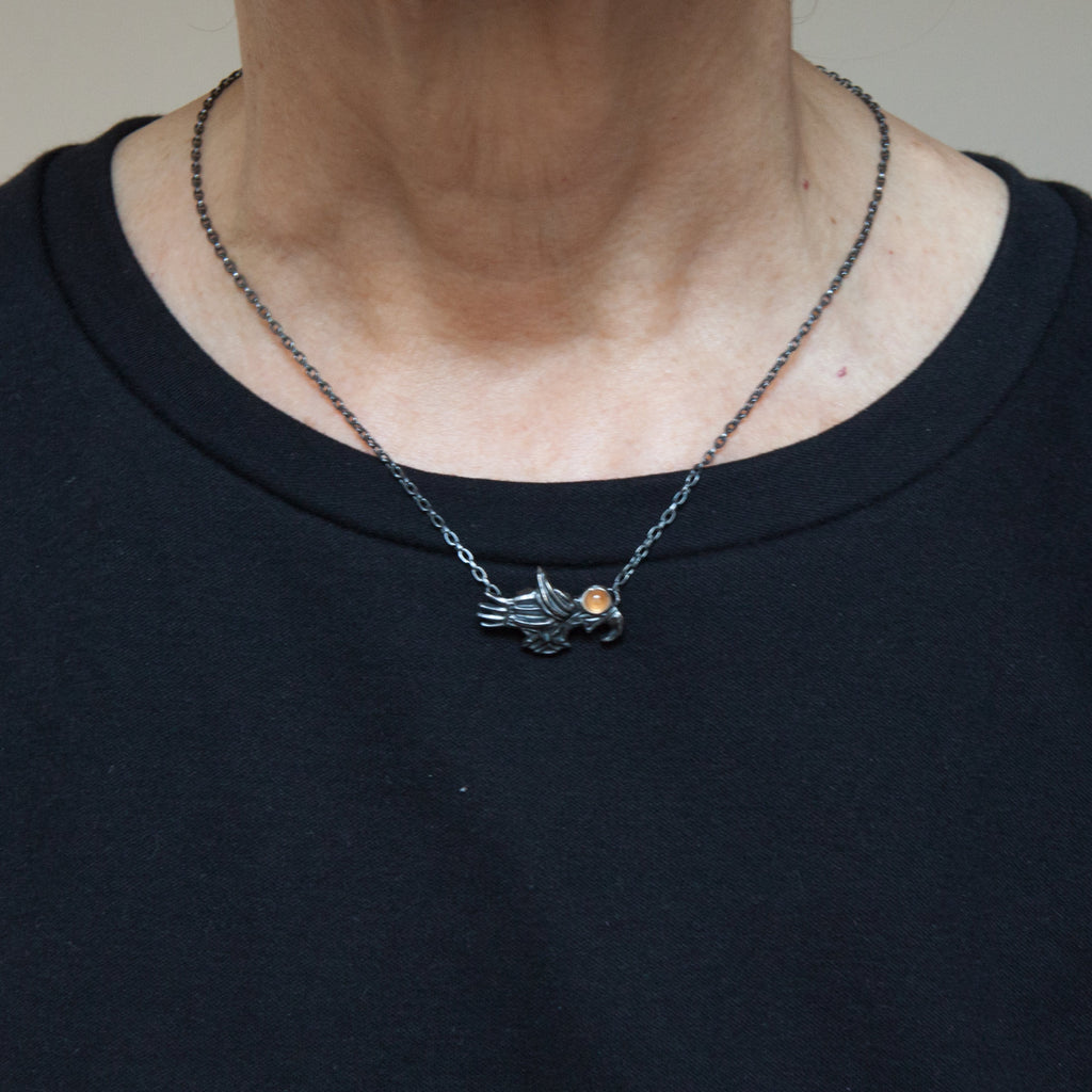 soaring bird silver necklace with a sapphire eye is shown being worn.