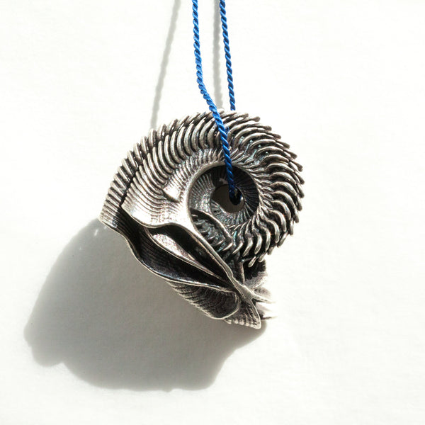 silver alien shell hanging from blue silk cord