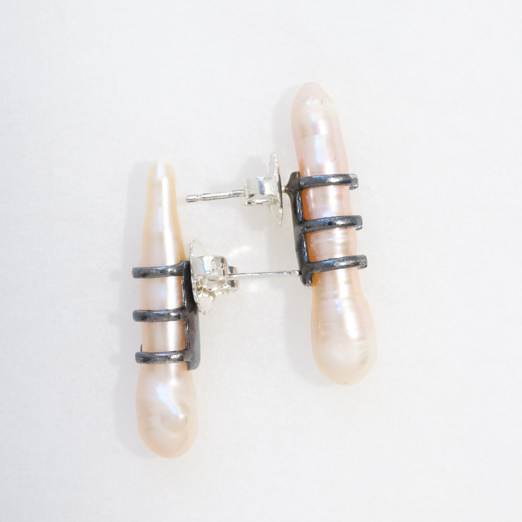 whimsical baroque pearl earrings with a blackened silver mount that looks like shoe laces. side view