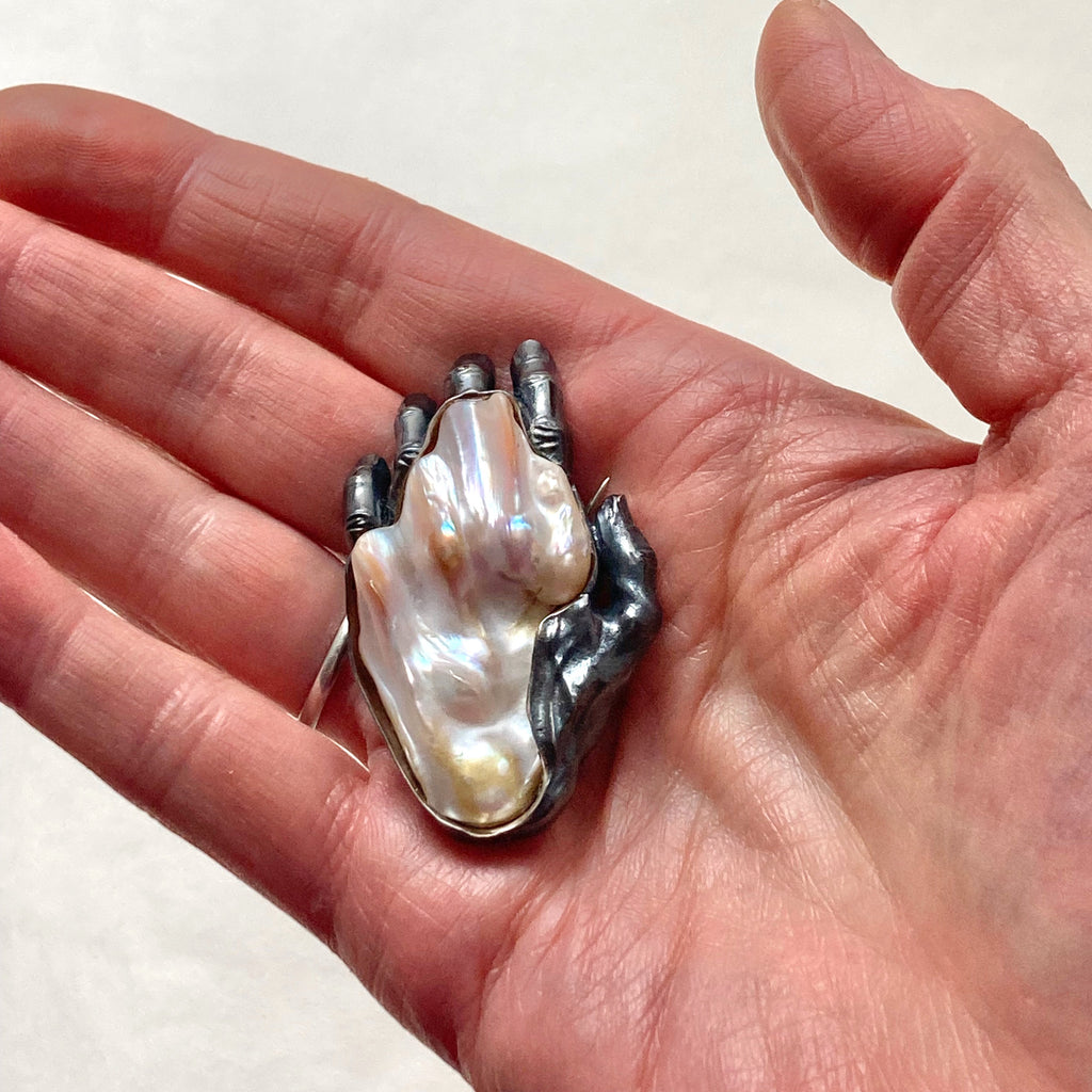 A baroque pearl as the back of a blackened silver left hand brooch. on a hand