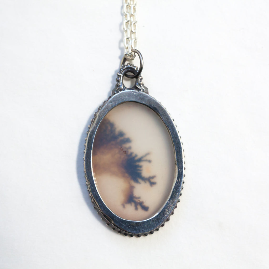 Lace-like dendritic agate in a victorian style silver frame on a silver chain. Back view