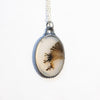 Lace-like dendritic agate in a victorian style silver frame on a silver chain. Front view