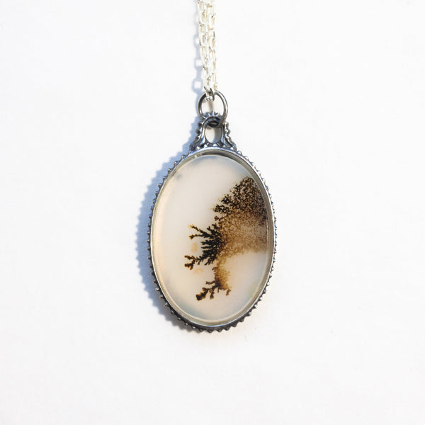 Lace-like dendritic agate in a victorian style silver frame on a silver chain. Front view