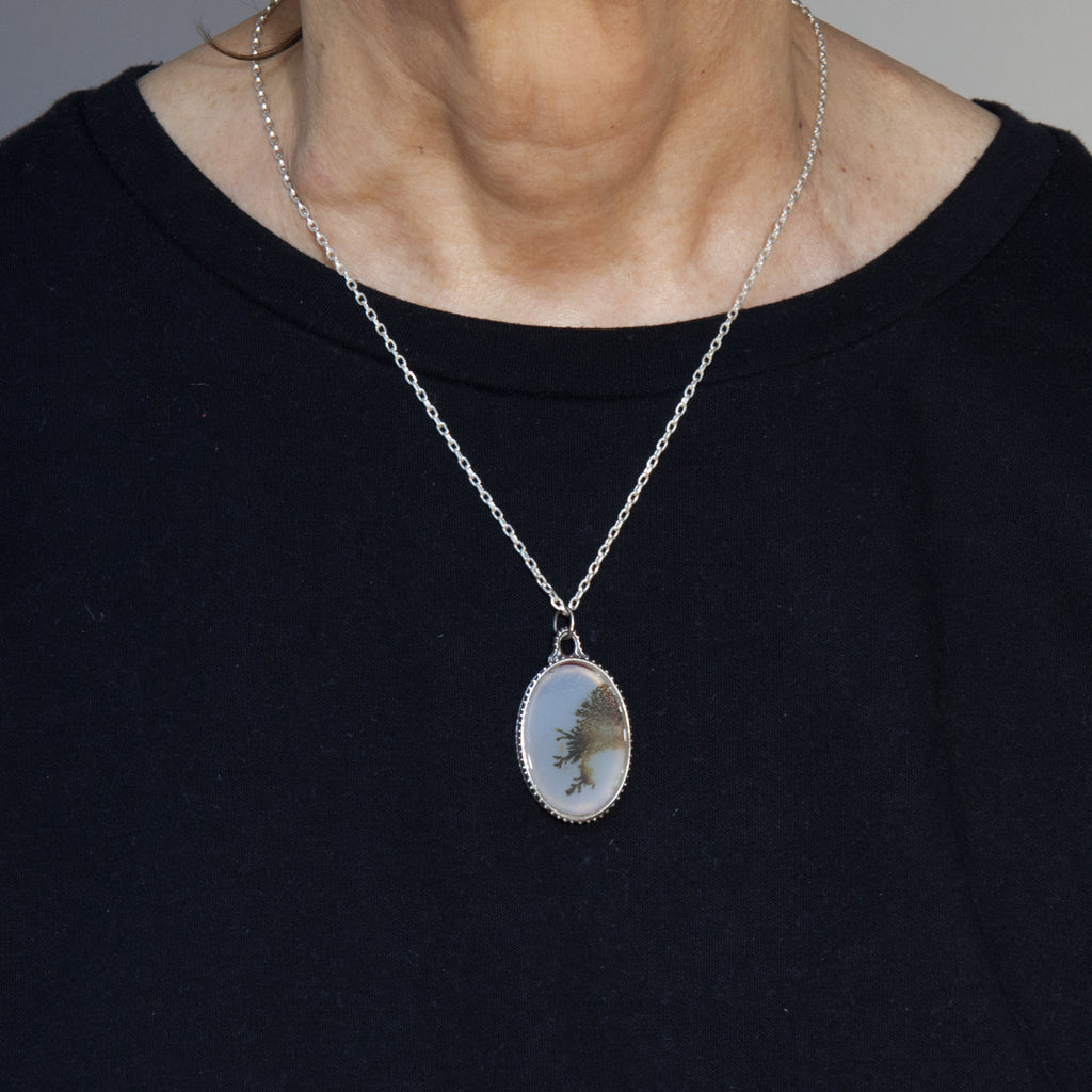 Lace-like dendritic agate in a victorian style silver frame on a silver chain. seen as worn.