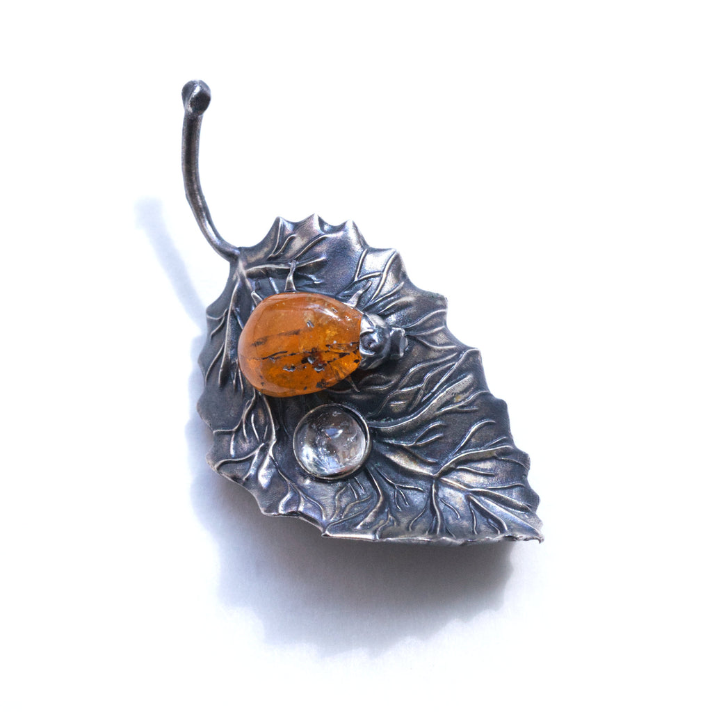 spessartite garnet ladybug on a sterling silver leaf blackened with liver of sulfur, and a topaz dewdrop. Front