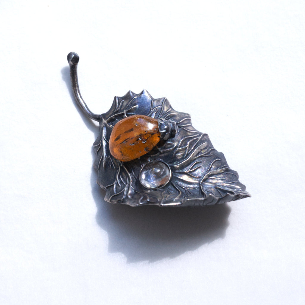 spessartite garnet ladybug on a sterling silver leaf blackened with liver of sulfur, and a topaz dewdrop. Front