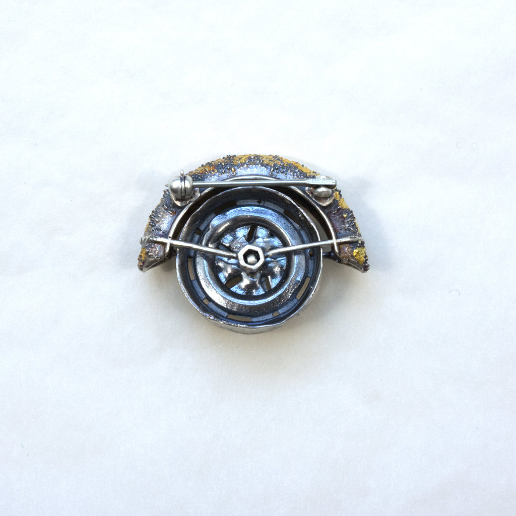 Lux fender brooch pendant with a pink spinel , blackened ssilver. 24k gold fused using keum boo process. The hubcap spins. back as brooch.