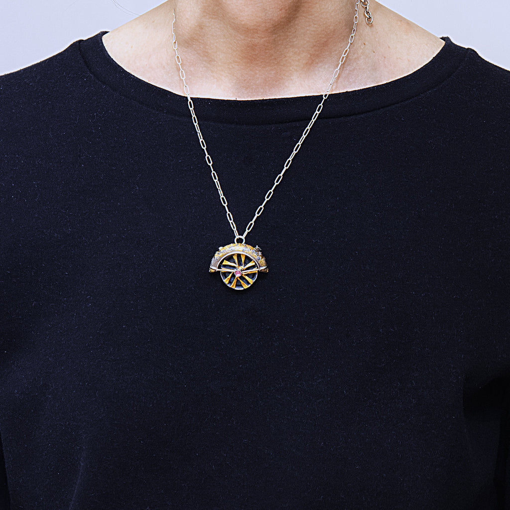 Lux fender brooch pendant with a pink spinel , blackened ssilver. 24k gold fused using keum boo process. The hubcap spins.As worn.