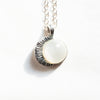 A closeup of the moonstone moon silver necklace with a shadow