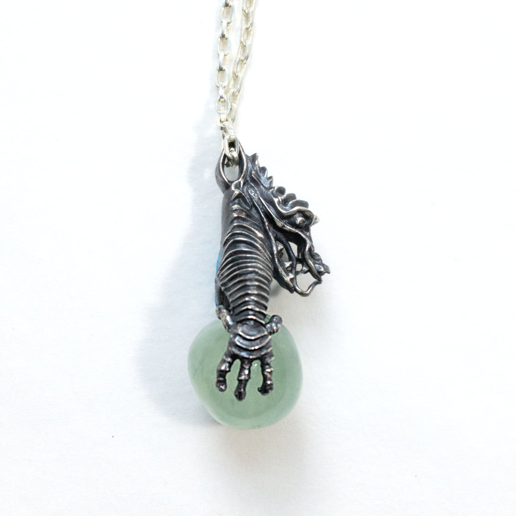 A dragon holding a prehnite sphere like he just caught it. Blackened silver, with a silver chain, side