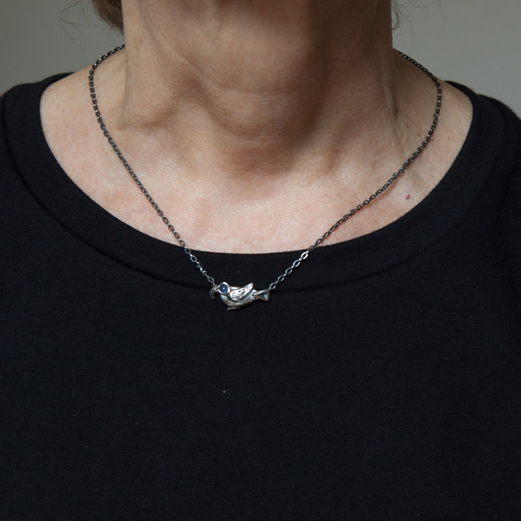 roosting bird silver necklace with a sapphire eye is shown being worn.