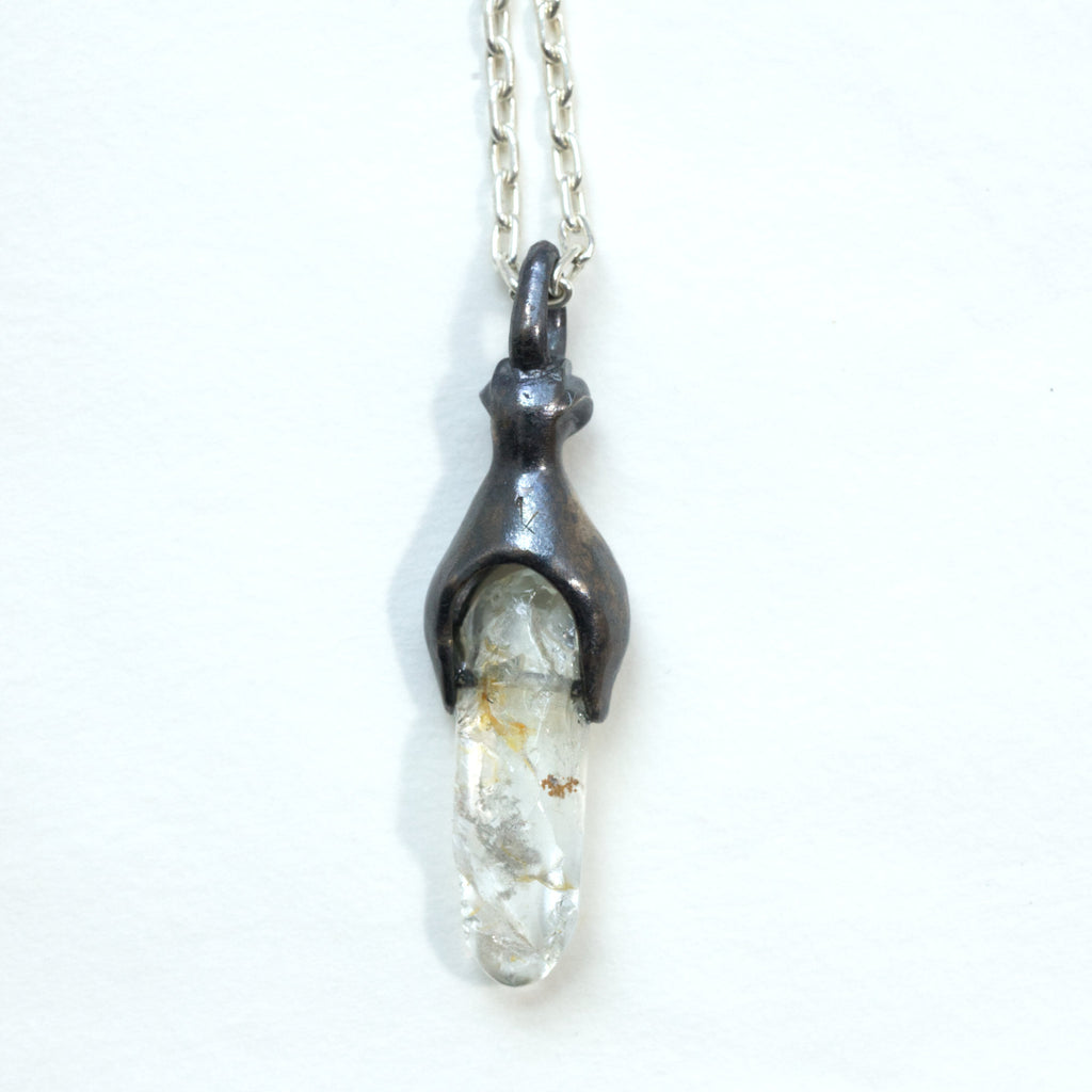 A white topaz with inclusions in a  blackened silver baby monster mount and 18" silver chain, back view.