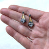 Grey spinel tri post back earrings. Blackened siver 24k gold foil fused to the silver. triangular grey spinel. on a hand to see the size.