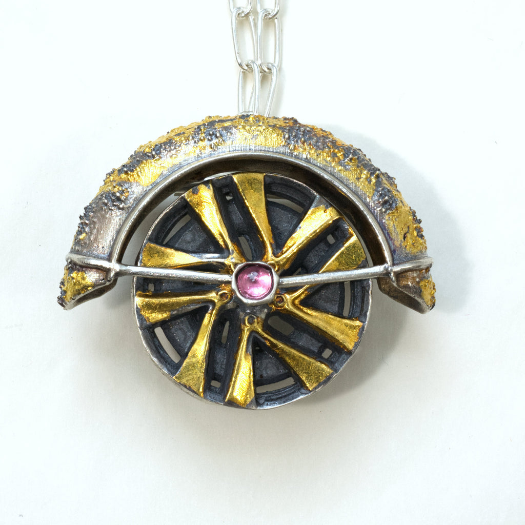 Lux fender brooch pendant with a pink spinel , blackened ssilver. 24k gold fused using keum boo process. The hubcap spins. Front with chain.
