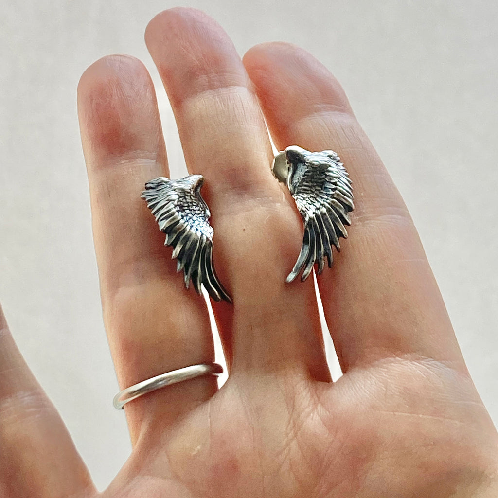 sterling silver wing earrings shown in a hand for size comparison