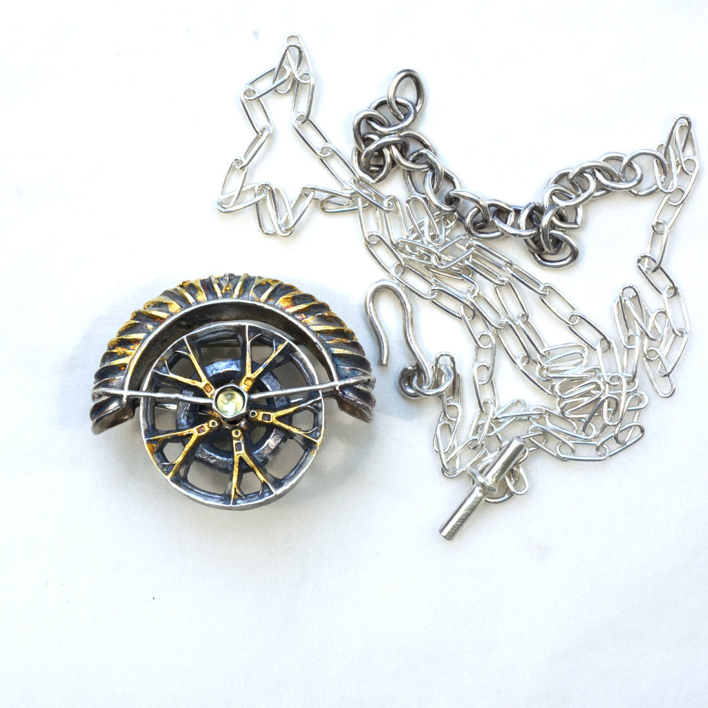 yaya fender brooch pendant. Blackened sterling silver, 24k gold foil applied using keum boo. Tthe hubcap spins. Front whit chain on the side.